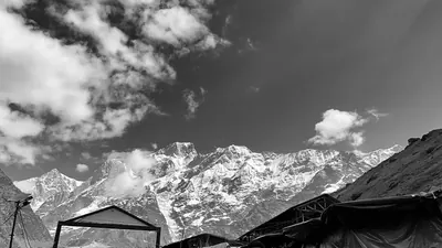 Black-and-white photograph of snow-covered mountains and clouds above dark shelter roofs.