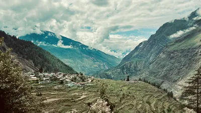 Terraced green fields and a small settlement sit between steep mountain walls under layered clouds.
