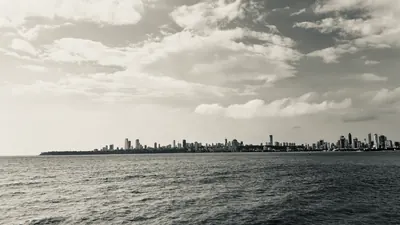 A faraway coastal skyline stretches across a monochrome sea beneath sunlit clouds.